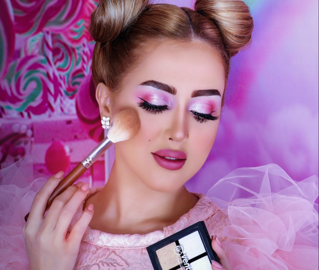 Woman wearing baby pink dress applying makeup foundation